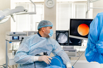 Obraz premium Medical specialists in modern operating room. Doctors perform a surgery and looking on the process on the monitor. Selective focus.