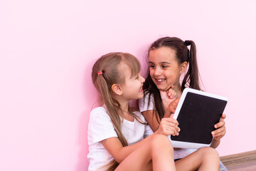 children, technology and home concept - two little girls with tablet pc computer on floor on a pink background