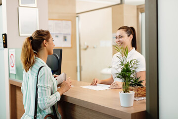 Happy woman talking to a receptionist while arriving at the spa. - obrazy, fototapety, plakaty