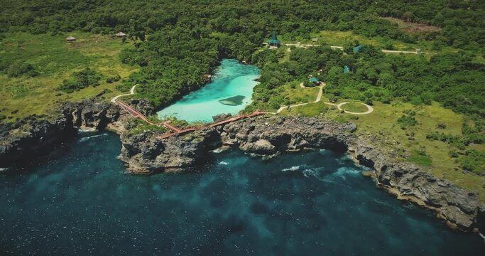 Azure lake on green rock coast at sea bay in aerial view. Tropical nature landscape of Sumba island, Indonesia. Beautiful salt water lagoon in greenery of trees and plants on cliffy sea shore