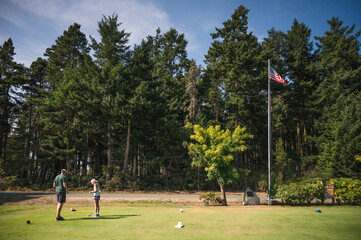 Man and young girl at golf tee with american flag and trees in background