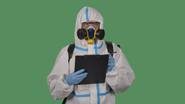 Portrait of a man in a protective suit, goggles, gloves and a respirator holds a folder and marks potentially dangerous places . Green screen, chroma key. Slow motion. Close up.
