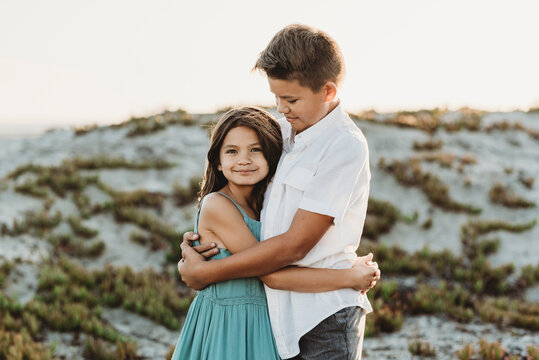 Preteen boy in white shirt hugging his younger sister at the beach
