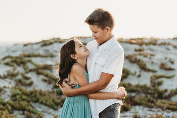 Preteen brother hugging younger sister at the beach