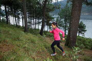 Mujer corriendo en el bosque, subiendo montañas con un lago al fondo