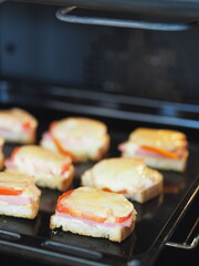 Hot homemade sandwiches with sausage, tomatoes and cheese on a baking sheet in the kitchen oven.Natural healthy food.