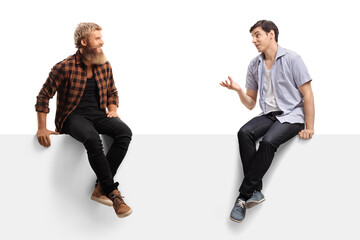 Two young men sitting on a blank panel and talking