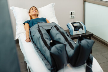 Relaxed woman enjoying in pressotherapy treatment at wellness center.