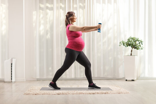Full length profile shot of a pregnant woman exercising with blue dumbbells