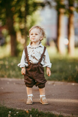 Fototapeta premium A small blond boy dressed in a vintage jumpsuit in a field at sunset