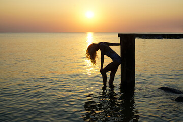 silhouette of  woman stands seashore. sunlight. girl enjoy sunny sunset. Blonde long hair.