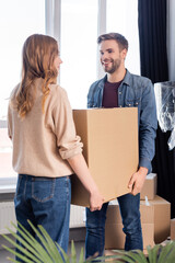 Fototapeta na wymiar joyful man looking at woman while holding carton box together, moving concept