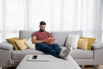 Young beautiful man or guy lying on the sofa at home reading the book and enjoying his free time without his wife and children with smile and happy face