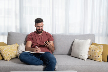 Young casual freelance man reading the text messages from his smart phone while he trying to work from home