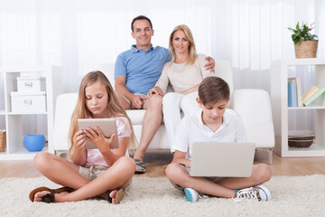 Children On The Carpet Using Tablet And Laptop