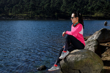 Atleta descansando a la orilla de un lago sentada sobre una piedra, después de correr en el bosque.