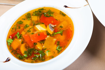 Traditional vegetable soup broth in a white plate on a table in a restaurant.