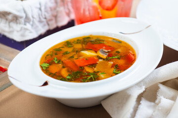 Traditional vegetable soup broth in a white plate on a table in a restaurant.