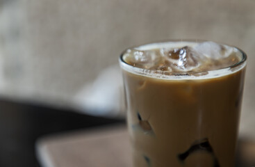 Cold coffee in a tall glass with ice cubes on wooden background. Cold summer drink on a black background with copy space. Focus and blur.