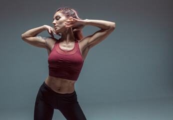 Portrait of a modern young girl performing elements of contemporary dance on a gray background.