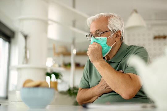Senior man coughing while wearing protective face mask at home.