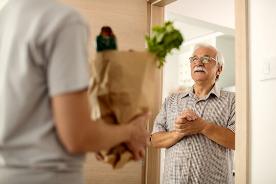 Happy senior man receiving groceries delivery at home.