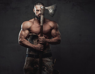 Brutal and powerful viking warrior with dreadlocks and beard posing with axe which covers half of his face in dark background.