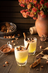 Refreshing delicious melon smoothie with cinnamon, hazelnuts and chocolate, vase of chrysanthemums and glasses of smoothie on wooden background