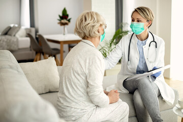 Happy female doctor wearing face mask while talking to mature woman at home.