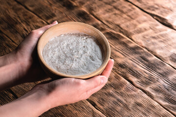 A flour in the wooden plate in the female hands close up on the kitchen table background.