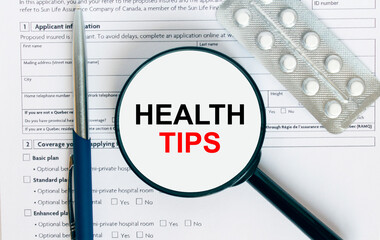 Magnifying glass with text Health Tips inside lies on medical documents with pills and a blue metal pen