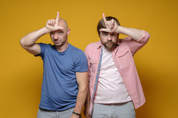 Two serious men in casual clothes are making mocking of someone by making a loser gesture with...