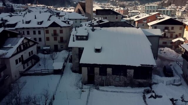 Pellizzano small mountain village buildings and church covered in winter snow, aerial reveal