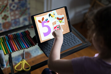 Looking down caucasian child young girl study desk learning school home computer tablet hand touch explore numbers 5 maths