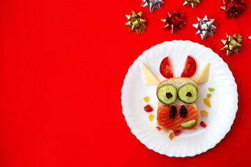 Funny sandwich with edible symbol of 2021 bull cow made from toast bread, red fish, cucumber, tomato, cheese and raisins. Breakfast idea for kids. christmas food top view , food art.
