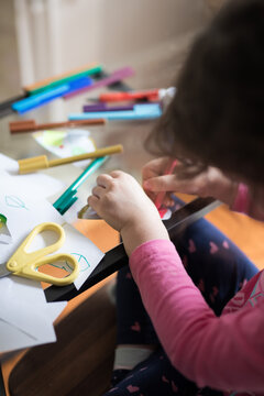 Looking Down At A Young Girl Child Seated At Her Study Desk Learning School From Home With Ipad Tablet Education Program Colored Colorful Textas Scissors Glue