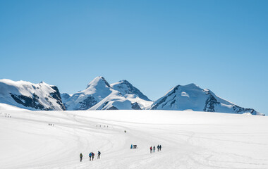 Mountainers crossing glacial plateu surrounded with Alpine peaks.
