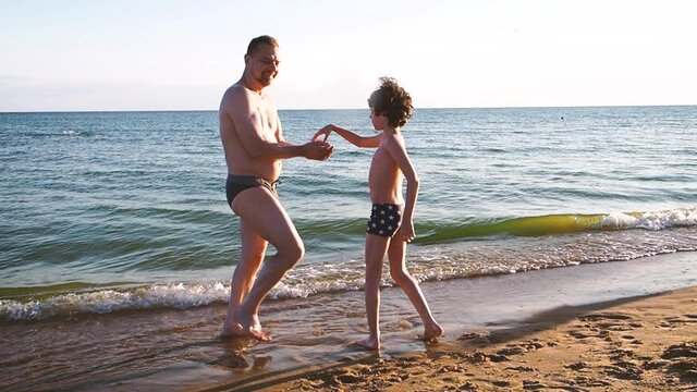 Father and little son having fut at seaside during summer vacations. Adult man and young boy in swimming trunks throwing stones into sea water cheerfully. Happy family concept. Teamwork concept