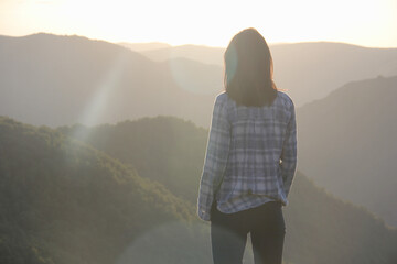 Young woman in gold sunset light looking far away against the backdrop of mountains.