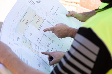 Workers' hands pointing to building plans at a construction site