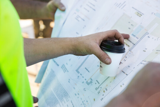 Workers' Hands On Building Plans At A Construction Site