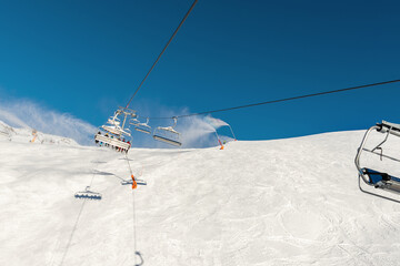 Scenic panoramic view of alpine peaks with ski lift ropeway on hilghland mountain winter resort and snow making machines on bright cold sunny day. downhill slopes with people and clear blue sky