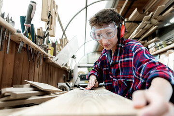 Young attractive 30-40 professional female carpenter looking grinding raw wood with sandpaper in carpentry diy workshop. Feminine women equality concept. Adult girl with male hobby at workbench