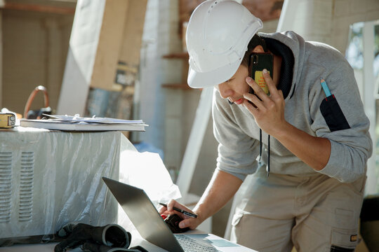 Man working on laptop while talking on smartphone at construction site