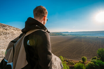 Young man in jacket standing admiring a mountaintop view looking out over distant ranges of...