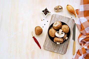 Whole and cut brown mushrooms in a clay bowl on a light concrete background. Cooking ingredients. Culinary background.