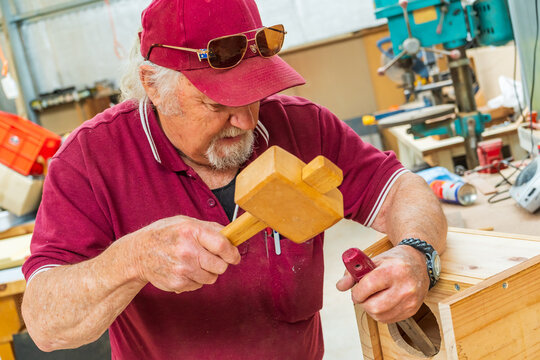 Close up of an elderly handyman using a mallet and chisel on a piece of woodwork in a Men's shed