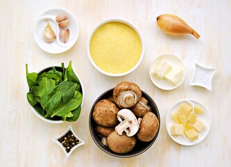 Prepared ingredients for cooking polenta with fried mushrooms and stewed spinach on a light concrete background. Step by step recipes. Polenta and corn grits recipes.