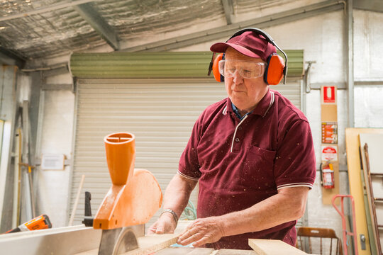 An elderly man sawing a piece of wood at a Men's shed.