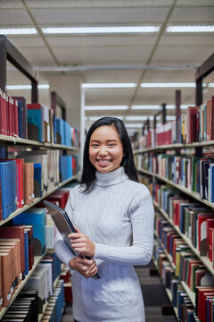 Young Asian student standing in aisle at university library